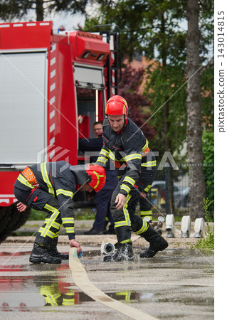 Firefighters Working Together With Fire Hose Beside Red Fire Truck During Emergency Response Training Firefighters Working Together With Fire Hose Beside Red Fire Truck During Emergency Response Training 143014815
