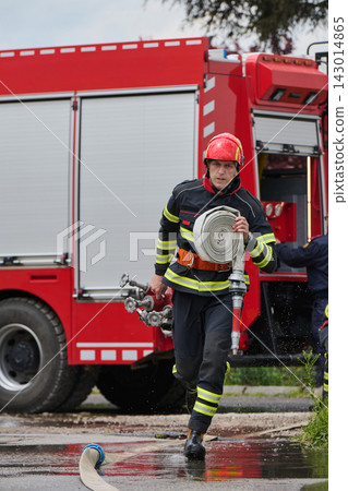 Firefighter Running With Rolled Fire Hose And Nozzle Beside Red Fire Truck During Emergency Response Firefighter Running With Rolled Fire Hose And Nozzle Beside Red Fire Truck During Emergency Response 143014865