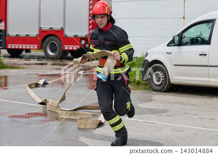 Firefighter Running With Fire Hose During Emergency Response Near Fire Truck And Rescue Vehicle Firefighter Running With Fire Hose During Emergency Response Near Fire Truck And Rescue Vehicle 143014884