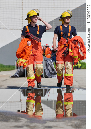 Two Firefighters in Orange Turnout Gear Walking Together During Training With Puddle Reflection Two Firefighters in Orange Turnout Gear Walking Together During Training With Puddle Reflection 143014922