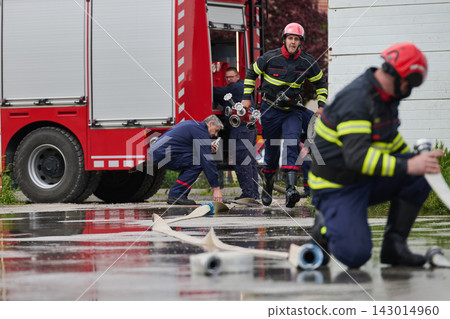 Firefighters Working Together Connecting Hoses by Red Fire Truck During Emergency Response Drill Firefighters Working Together Connecting Hoses by Red Fire Truck During Emergency Response Drill 143014960