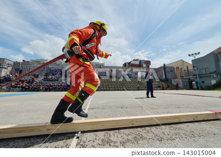 Firefighter Training Drill Balancing On Beam While Carrying Hose During Outdoor Emergency Exercise 143015004