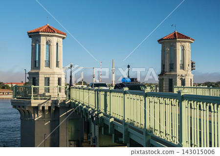 Two Mediterranean-style towers rise above the Bridge of Lions in Saint Augustine, Florida. Cars cross the green drawbridge beside blue water under a clear sky. Two Mediterranean-style towers rise above the Bridge of Lions in Saint Augustine, Florida. Cars cross the green drawbridge beside blue water under a clear sky. 143015006