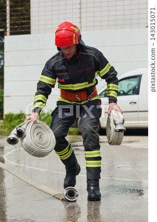 Firefighter Carrying Rolled Fire Hoses Wearing Helmet And Protective Uniform During Emergency Drill 143015071