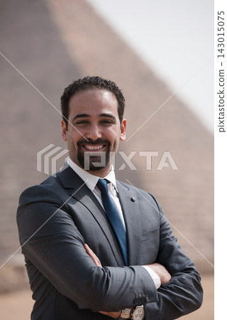 Confident Egyptian business executive in gray suit and navy tie smiling with arms crossed before the Giza pyramid backdrop ideal for MENA corporate Confident Egyptian business executive in gray suit and navy tie smiling with arms crossed before the Giza pyramid backdrop ideal for MENA corporate 143015075