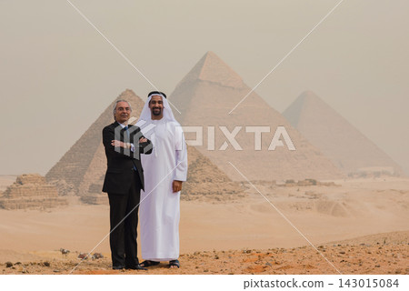 Confident multigenerational Arab business partners in traditional kandura and formal dark suit standing side by side at the iconic Great Pyramids of Confident multigenerational Arab business partners in traditional kandura and formal dark suit standing side by side at the iconic Great Pyramids of 143015084