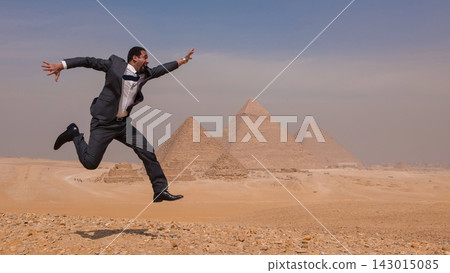 Triumphant middle eastern businessman in gray suit captured mid air leap against all three Giza Pyramids on sunny Egyptian desert plateau ideal for Triumphant middle eastern businessman in gray suit captured mid air leap against all three Giza Pyramids on sunny Egyptian desert plateau ideal for 143015085