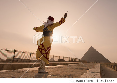 Traditional Egyptian tanoura dancer in ornate yellow embroidered costume and red fez spinning dramatically before the Great Pyramid of Giza under a Traditional Egyptian tanoura dancer in ornate yellow embroidered costume and red fez spinning dramatically before the Great Pyramid of Giza under a 143015237