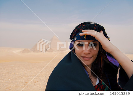 Intimate portrait of a confident young Egyptian woman in ornate traditional coin headwrap smiling directly at camera with the iconic three Giza Intimate portrait of a confident young Egyptian woman in ornate traditional coin headwrap smiling directly at camera with the iconic three Giza 143015289
