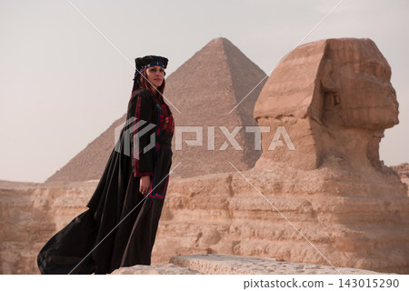 Cinematic portrait of a woman in ornate embroidered folk costume glancing back beside the Great Sphinx and pyramid at Giza Egypt ideal for luxury Cinematic portrait of a woman in ornate embroidered folk costume glancing back beside the Great Sphinx and pyramid at Giza Egypt ideal for luxury 143015290