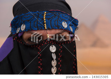 Authentic bedouin woman wearing ornate embroidered niqab and blue headband adorned with silver Eye of Horus coins delivering a piercing intense gaze Authentic bedouin woman wearing ornate embroidered niqab and blue headband adorned with silver Eye of Horus coins delivering a piercing intense gaze 143015305