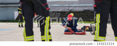 Firefighter Training Drill With Kneeling Firefighter Connecting Hose During Team Exercise Firefighter Training Drill With Kneeling Firefighter Connecting Hose During Team Exercise 143015314