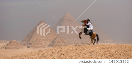 Powerful arab horseman riding a rearing arabian horse on the Giza plateau with two Great Pyramids of Giza behind him under overcast desert haze Egypt Powerful arab horseman riding a rearing arabian horse on the Giza plateau with two Great Pyramids of Giza behind him under overcast desert haze Egypt 143015332