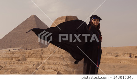 Abaya caught mid flight by desert wind as a young Arab woman stands confidently before the Great Sphinx and Great Pyramid on the Giza plateau in Egypt Abaya caught mid flight by desert wind as a young Arab woman stands confidently before the Great Sphinx and Great Pyramid on the Giza plateau in Egypt 143015343
