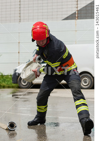 Firefighter Rolling Hose During Emergency Response Training With Protective Helmet And Reflective Gear 143015461