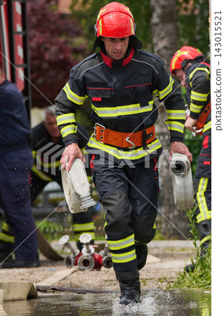 Firefighter Running With Water Hoses During Emergency Response Training In Protective Gear 143015521