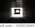 Dark concrete pedestrian tunnel with bright rectangular exit framed by linear wall lights, strong shadows, and deep perspective toward walkway in urban night scene 143015649