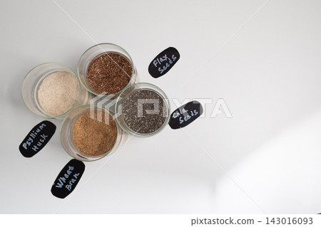 Dry seeds and grains in glass jars on a white studio surface top view Dry seeds and grains in glass jars on a white studio surface top view 143016093