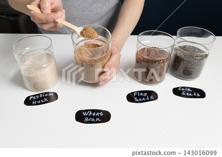 Scooping high fiber ingredients into a glass jar on a clean white kitchen counter Scooping high fiber ingredients into a glass jar on a clean white kitchen counter 143016099