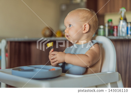 Infant practices self feeding with vegetables in a kitchen, showing baby led weaning, early nutrition and family care concept 143016110