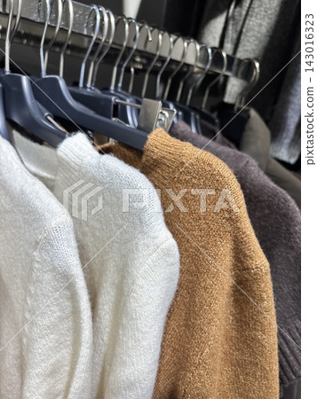Close up of camel brown and white knitted sweaters hanging on rack in clothing store, warm neutral autumn winter fashion collection Close up of camel brown and white knitted sweaters hanging on rack in clothing store, warm neutral autumn winter fashion collection 143016323