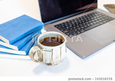 一台筆記型電腦、一杯咖啡和一本藍色封面的書。 一台筆記型電腦、一杯咖啡和一本藍色封面的書。 143016559