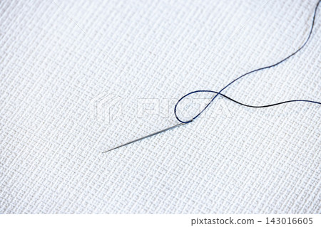 A metal sewing needle with thread placed on a white piece of cloth. A metal sewing needle with thread placed on a white piece of cloth. 143016605