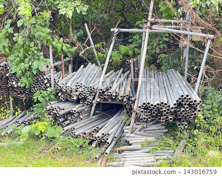 A large quantity of old metal pipes stored outdoors in a green area. A large quantity of old metal pipes stored outdoors in a green area. 143016759