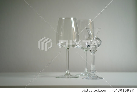 Bare wine glasses and a glass decanter stand on a white table. Concept of elegance, dining, hospitality, minimalism, still life, refinement and taste Bare wine glasses and a glass decanter stand on a white table. Concept of elegance, dining, hospitality, minimalism, still life, refinement and taste 143016987