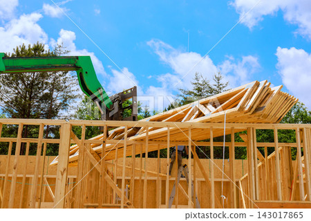 Crane is lifting wooden trusses beams to top of building frame on residential construction Crane is lifting wooden trusses beams to top of building frame on residential construction 143017865