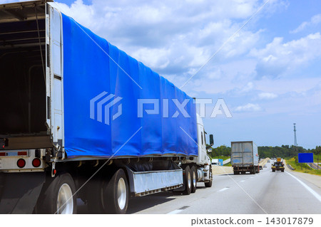 Trucks move along highway in rural area with blue tarps covering their cargo Trucks move along highway in rural area with blue tarps covering their cargo 143017879