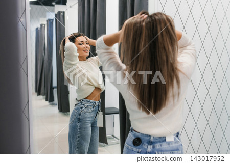 Smiling Woman Adjusting Hair While Trying On Jeans Smiling Woman Adjusting Hair While Trying On Jeans 143017952