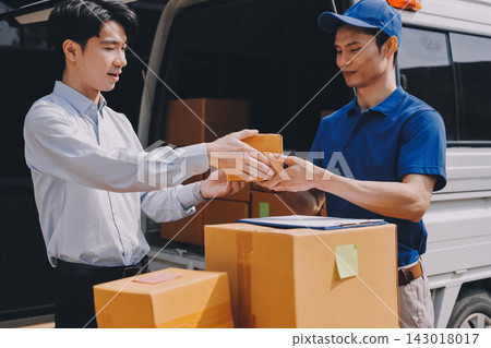 Young businessman signing a delivery receipt document on a clipboard held by a courier in a blue uniform. 143018017