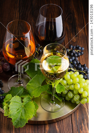 Three glasses of wine and fresh grapes arranged on a metallic tray with wooden background Three glasses of wine and fresh grapes arranged on a metallic tray with wooden background 143018196