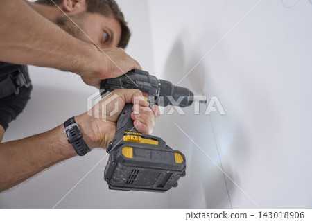 Man drills hole in white interior wall with cordless power drill Man drills hole in white interior wall with cordless power drill 143018906