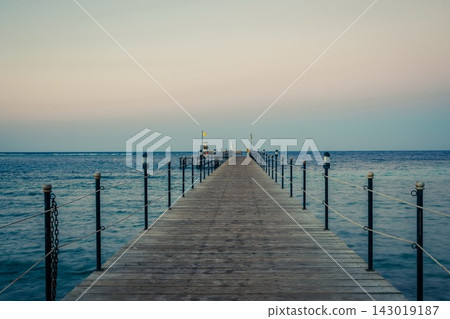 Wooden pier at sunrise in the tropical sea. Palm trees in the distance. Beautiful wooden pier. Long exposure of the sea as a haze Wooden pier at sunrise in the tropical sea. Palm trees in the distance. Beautiful wooden pier. Long exposure of the sea as a haze 143019187