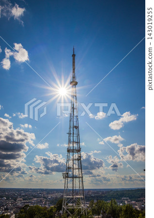 Metallic lattice communication tower in blue sky with sun starburst Metallic lattice communication tower in blue sky with sun starburst 143019255