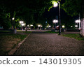 People sitting on stone benches in a park at night under streetlights 143019305