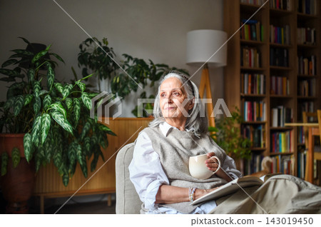 Peaceful senior woman relaxing with warm drink in cozy home. Peaceful senior woman relaxing with warm drink in cozy home. 143019450