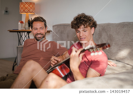Father teaching teenage son to play guitar at home. Father teaching teenage son to play guitar at home. 143019457