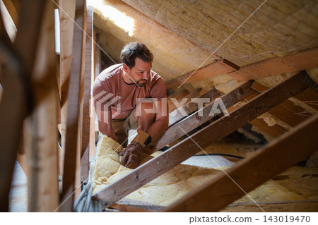 Homeowner insulating attic during home renovation project. Homeowner insulating attic during home renovation project. 143019470