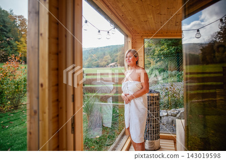 Elderly woman relaxing in wooden sauna cabin with countryside view. Elderly woman relaxing in wooden sauna cabin with countryside view. 143019598