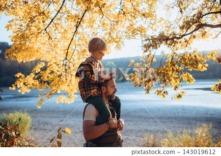 Father carrying young son on shoulders during autumn walk by lake. Father carrying young son on shoulders during autumn walk by lake. 143019612
