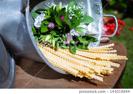 Fresh mixed flower bouquet with green foliage arranged inside metal container on wooden table, with soft outdoor sunlight, colorful petals, rustic presentation, natural garden celebration mood Fresh mixed flower bouquet with green foliage arranged inside metal container on wooden table, with soft outdoor sunlight, colorful petals, rustic presentation, natural garden celebration mood 143019844