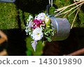 Rustic metal cup hanging with small colorful flower arrangement and soft green blurred background, creating delicate decorative detail with sunlight, natural textures, and elegant handmade garden 143019890