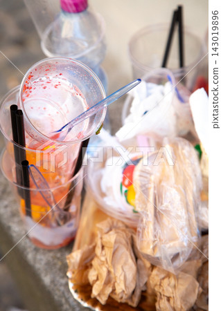 Discarded disposable cups, straws, crumpled paper, and food packaging scattered together on stone surface after outdoor gathering, highlighting messy cleanup, waste, and litter Discarded disposable cups, straws, crumpled paper, and food packaging scattered together on stone surface after outdoor gathering, highlighting messy cleanup, waste, and litter 143019896