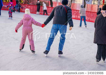 Father and Daughter Holding Hands While Ice Skating. Adult and child hold hands while , emphasizes family support, bonding and shared winter recreation Father and Daughter Holding Hands While Ice Skating. Adult and child hold hands while , emphasizes family support, bonding and shared winter recreation 143019986