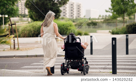 Caregiver pushing adult with spina bifida in wheelchair Caregiver pushing adult with spina bifida in wheelchair 143020282