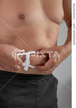 A man measures the amount of subcutaneous fat on his stomach using a caliper. A man measures the amount of subcutaneous fat on his stomach using a caliper. 143020748