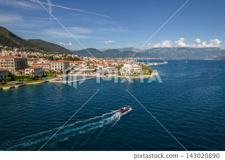 Aerial coastal view of a speedboat crossing the Bay of Kotor in front of One&Only Portonovi resort in Kumbor, Montenegro, backed by steep green mountains. Aerial coastal view of a speedboat crossing the Bay of Kotor in front of One&Only Portonovi resort in Kumbor, Montenegro, backed by steep green mountains. 143020890